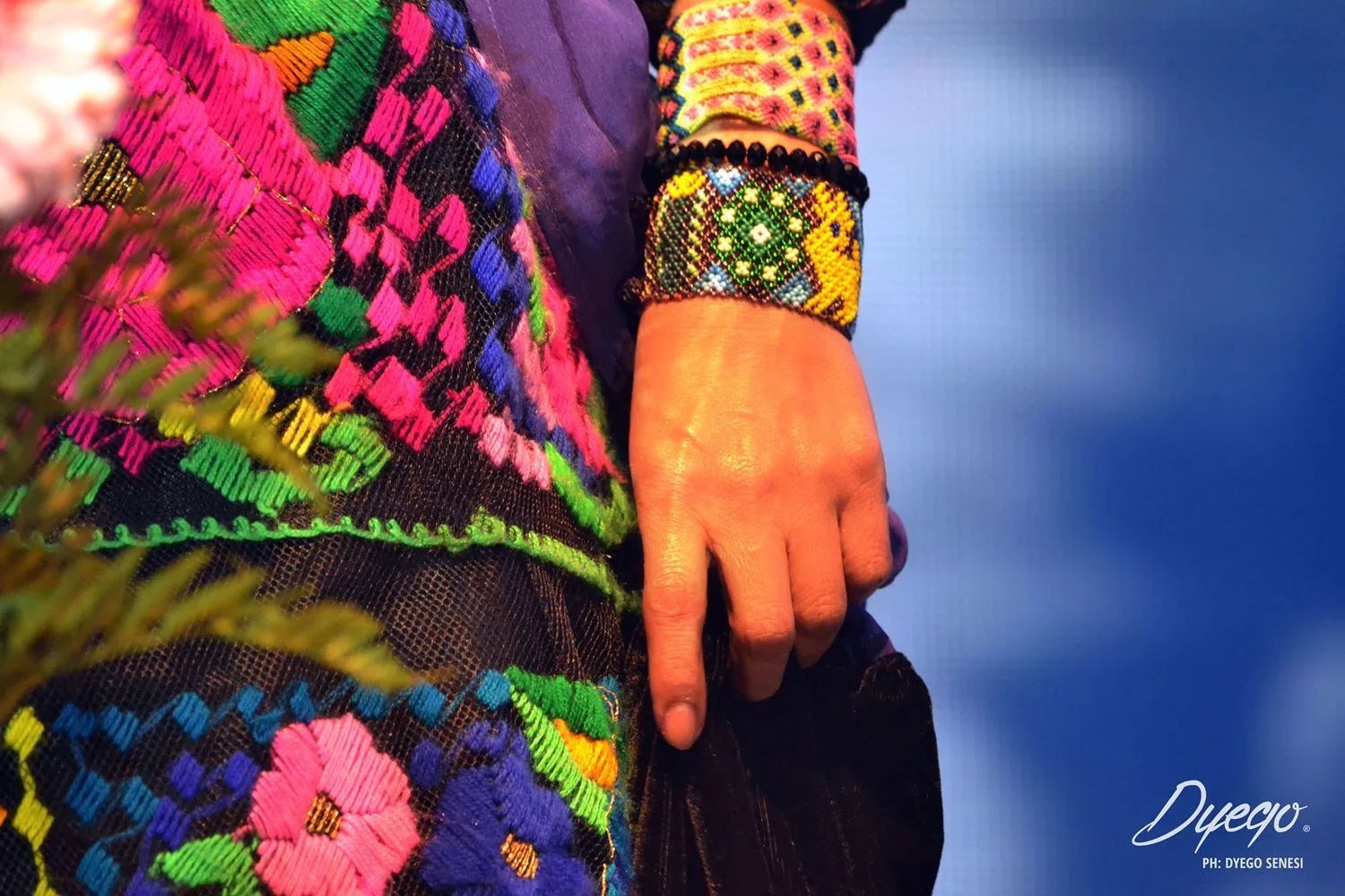 Detalle — mano, bordado y textura del vestuario
